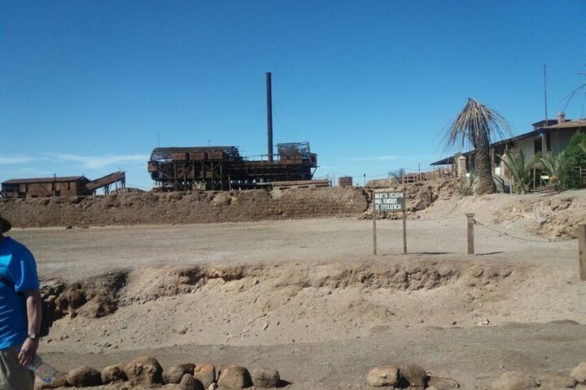 A construction site with a large building under construction, a tall chimney, and a sign indicating a mining area. 4