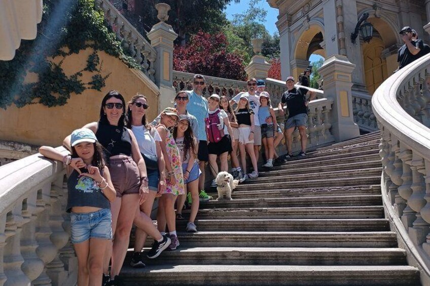 A group of people ascending a stone staircase with ornate railings, surrounded by greenery and architectural elements. 2