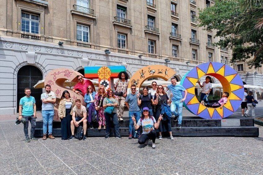 A group of people posing in front of a colorful sculpture with geometric shapes and a building in the background. 1