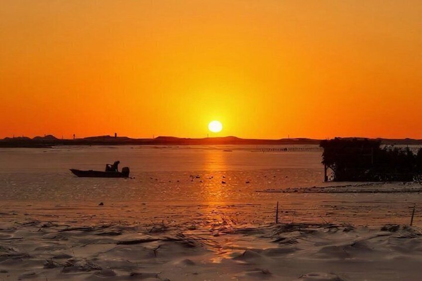 A sunset over a calm body of water with a boat and a distant shoreline. 2