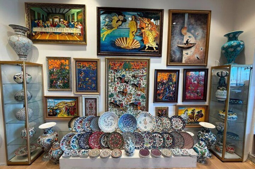 A display of colorful plates and vases in a shop with various framed artworks on the walls. 4