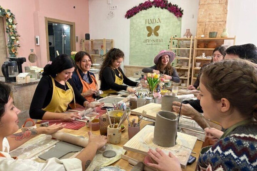 A group of people engaged in pottery making at a studio with a sign reading 'HADA artesana.' 1