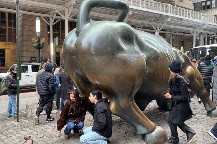 A large bronze bull sculpture in an urban setting with people around it. 1