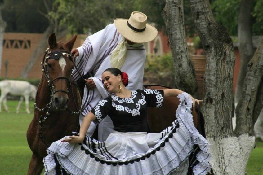 A person in traditional attire with a horse, trees, and a fence in the background. 1