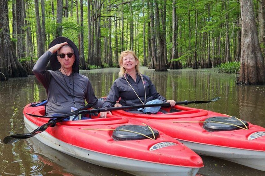 Two people in a red kayak on a calm river surrounded by a dense forest. 3