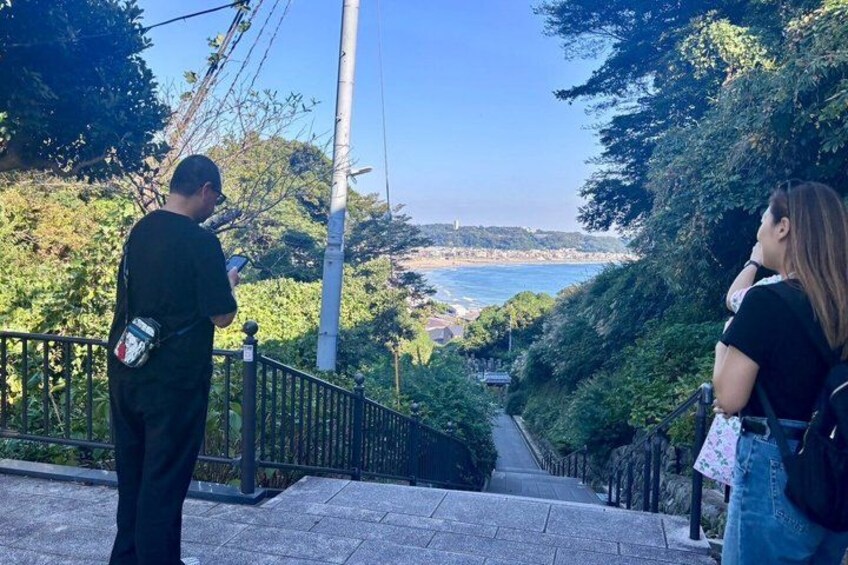 A person taking a photo with a smartphone, a railing, and a view of a coastal landscape. 4
