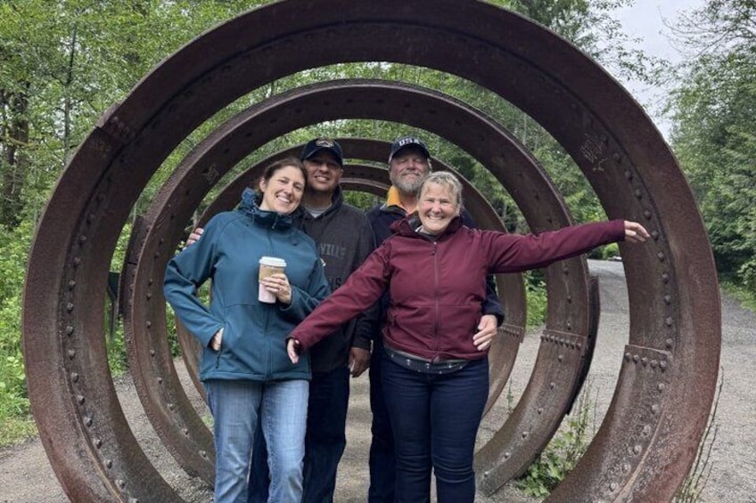 Three people standing in front of a large circular metal structure. 5