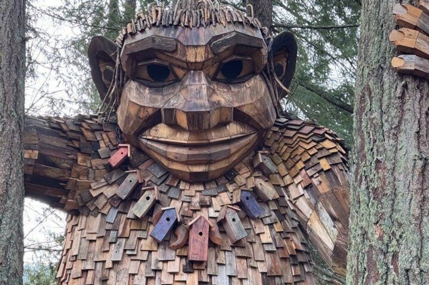 A wooden sculpture resembling a humanoid figure with a detailed face and a complex structure made of logs. 1