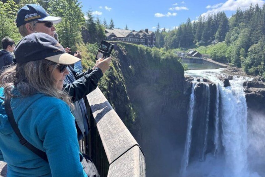 A waterfall with a viewing platform, surrounded by trees and a building in the background. 4