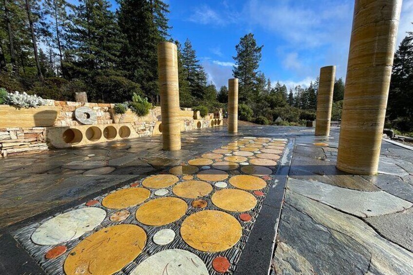 A mosaic pathway with circular patterns, stone columns, and a forested background. 5