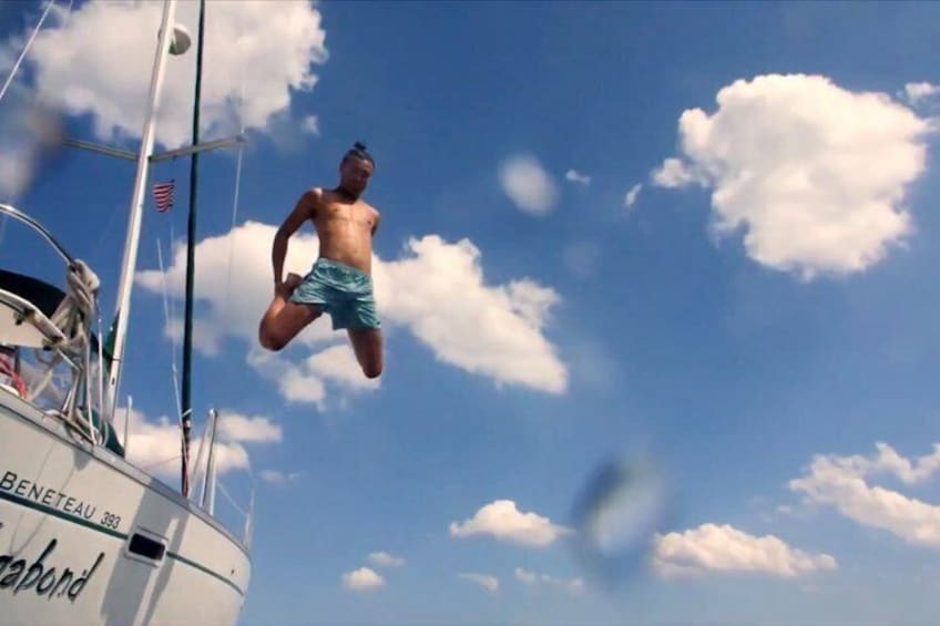 A person jumping off a boat named 'BENETEAU 389' with a clear blue sky and clouds in the background. 3