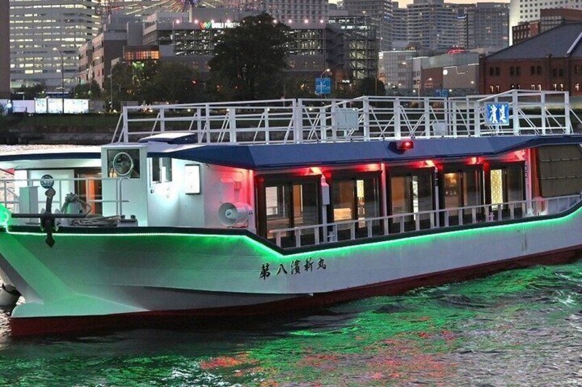 A boat with green lighting on its deck, a cityscape in the background, and Japanese characters on the side. 2