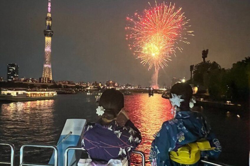 A boat with passengers enjoying a fireworks display over a city skyline. 1