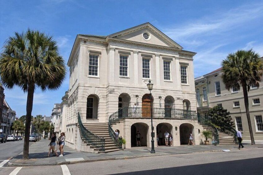 A historic building with a central pediment, arched windows, and a staircase leading to a balcony. 5
