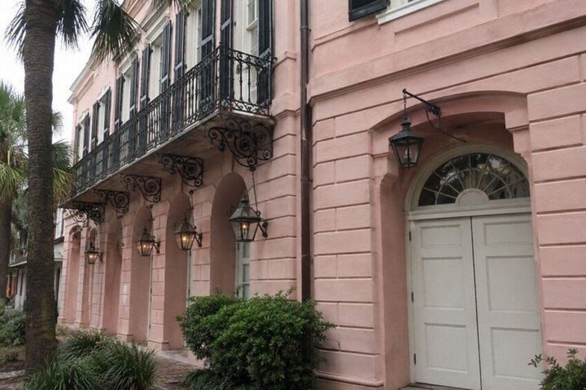 A pink building with a balcony, arched windows, and a white door. 3