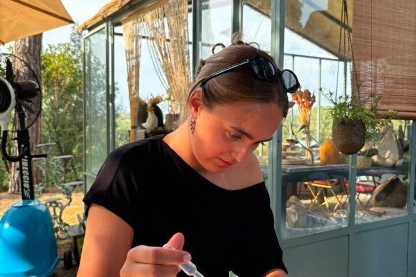 A person sitting indoors with a fan, holding a pen, and a window with plants in the background. 2
