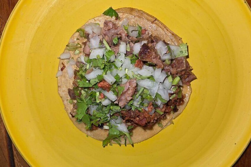 A yellow plate with a tortilla topped with diced onions, cilantro, and meat. 2