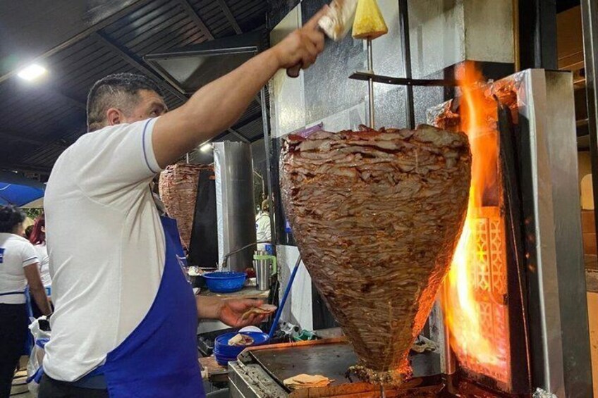 A person cooking meat on a vertical rotisserie. 1