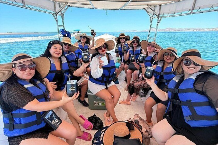 A group of people on a boat wearing life jackets, holding drinks, and enjoying the sea view. 2