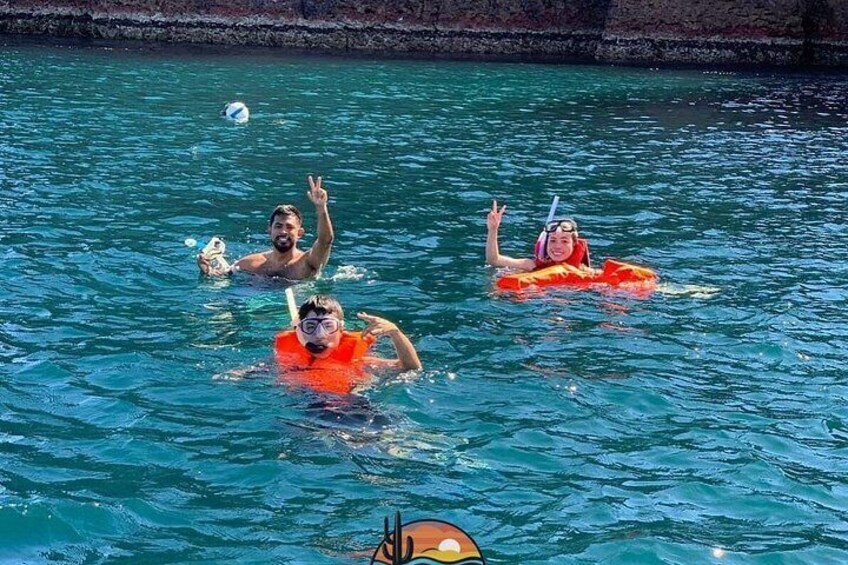 Three people swimming in a body of water, wearing life jackets. 5