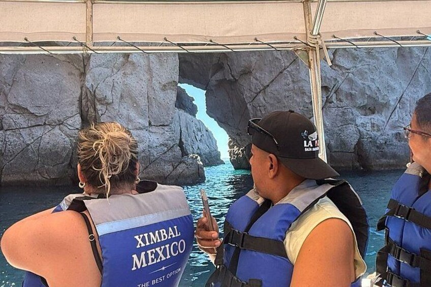 A group of people on a boat wearing life jackets, with a rocky coastline and a waterfall in the background. 3