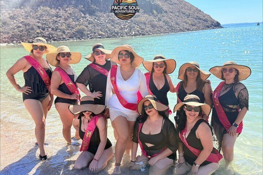 A group of people at a beach with clear water and a rocky island in the background. 3