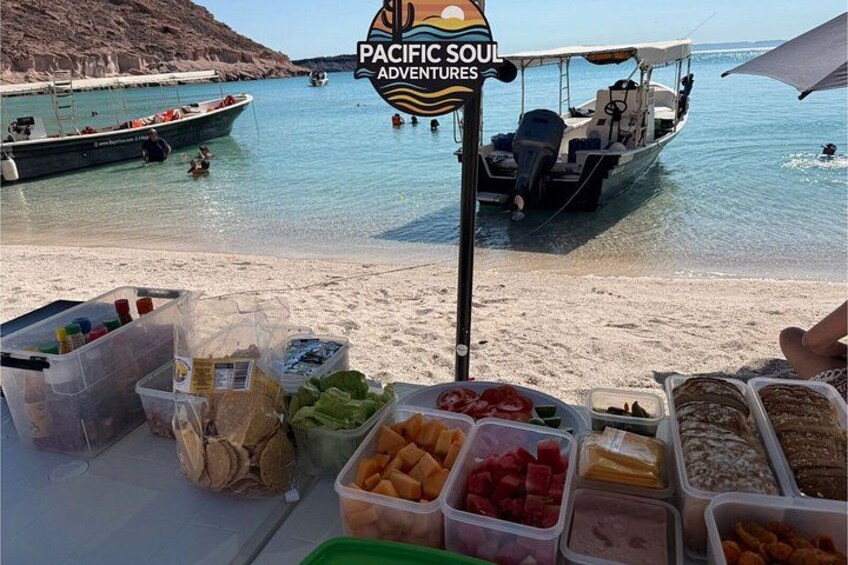 A beachside food stall with various food items and a boat in the background. 4