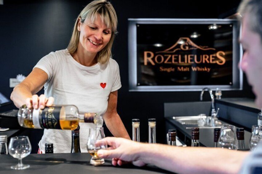 A person pouring a drink into a glass at a bar with a sign reading 'Rozelieures Single Malt Whisky'. 4