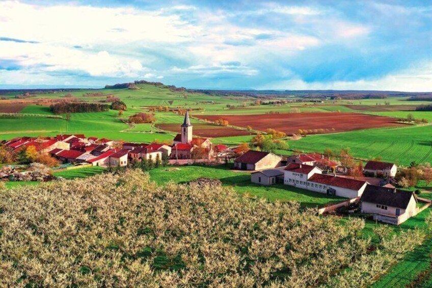 A rural village with red-roofed houses, a church, and expansive green fields. 1