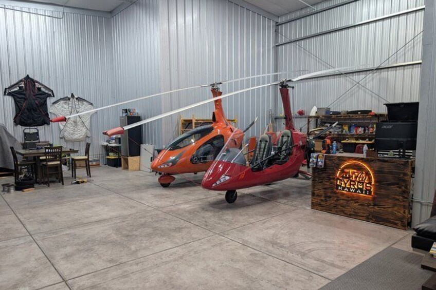 A red helicopter in a hangar with a neon sign reading 'Hawaii' and various equipment and tools around. 2