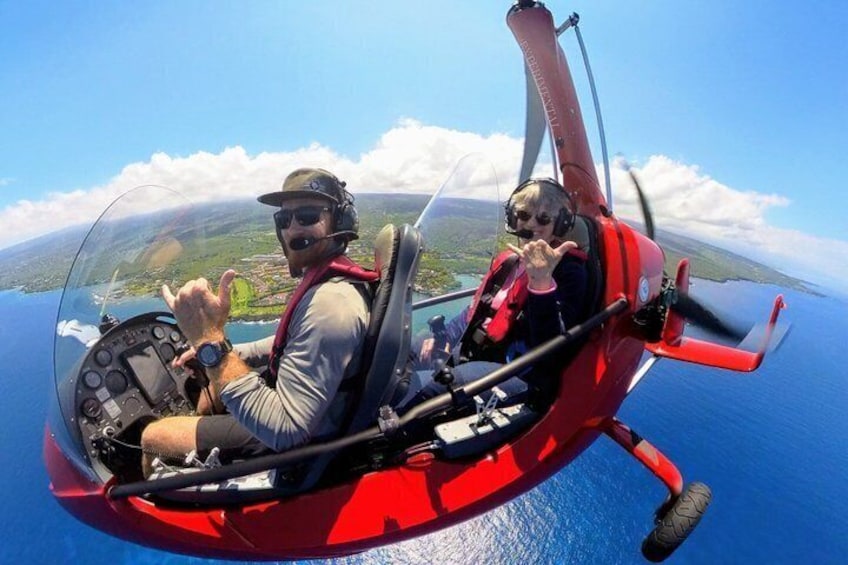 A person in a red helicopter cockpit with a clear view of the landscape below. 1