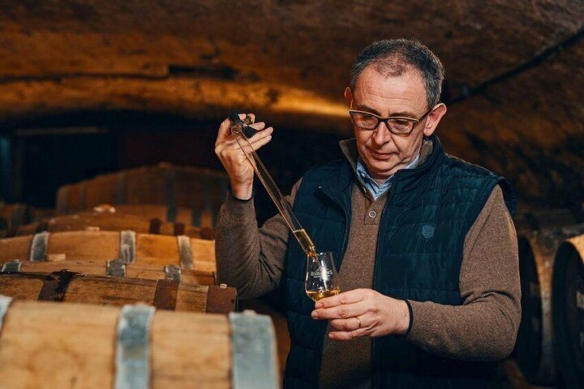 A person inspecting a wine bottle with a corkscrew in a cellar with wooden barrels. 4