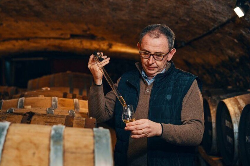 A person holding a wine glass and a magnifying glass in a cellar with wooden barrels. 1