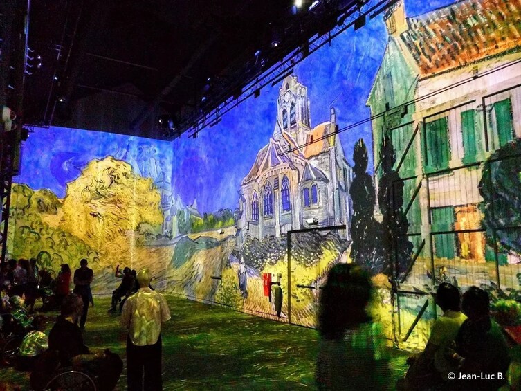 A large mural of a church and landscape, with people observing it. 2