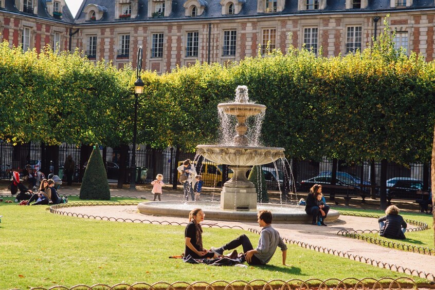 A public square with a central fountain, surrounded by a hedge and a row of parked cars. 5