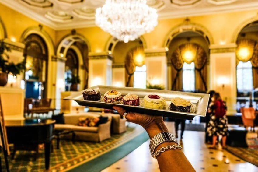 A person holding a tray with pastries in a grand, ornately decorated interior. 3