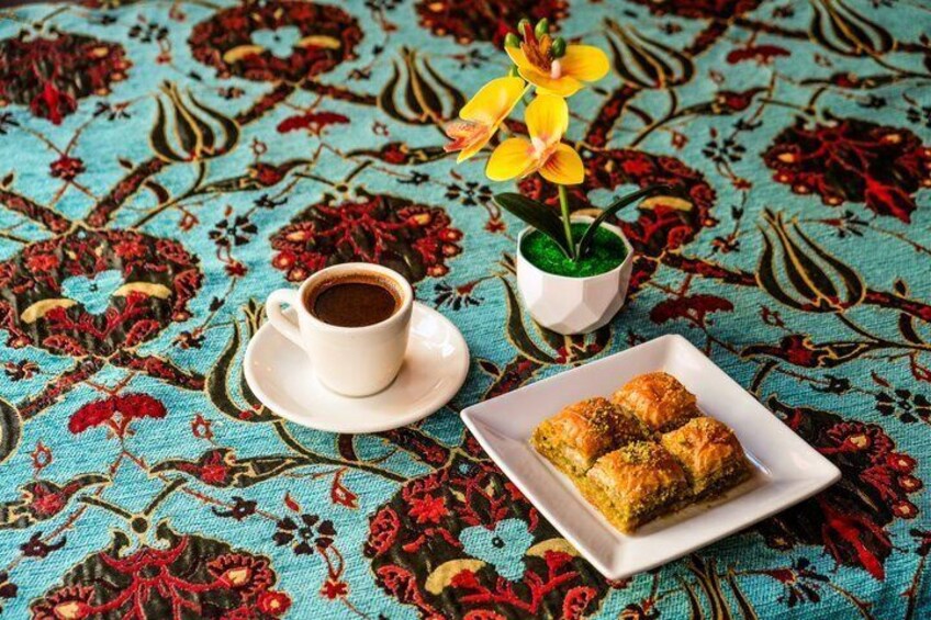 A cup of coffee, a plate of pastries, and a potted plant on a patterned tablecloth. 5