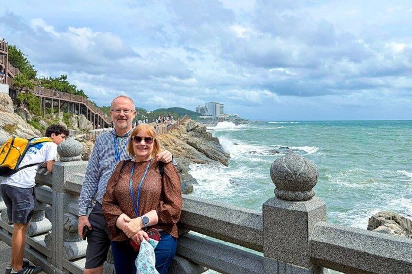 A coastal walkway with a railing, ocean waves, and a distant cityscape. 5