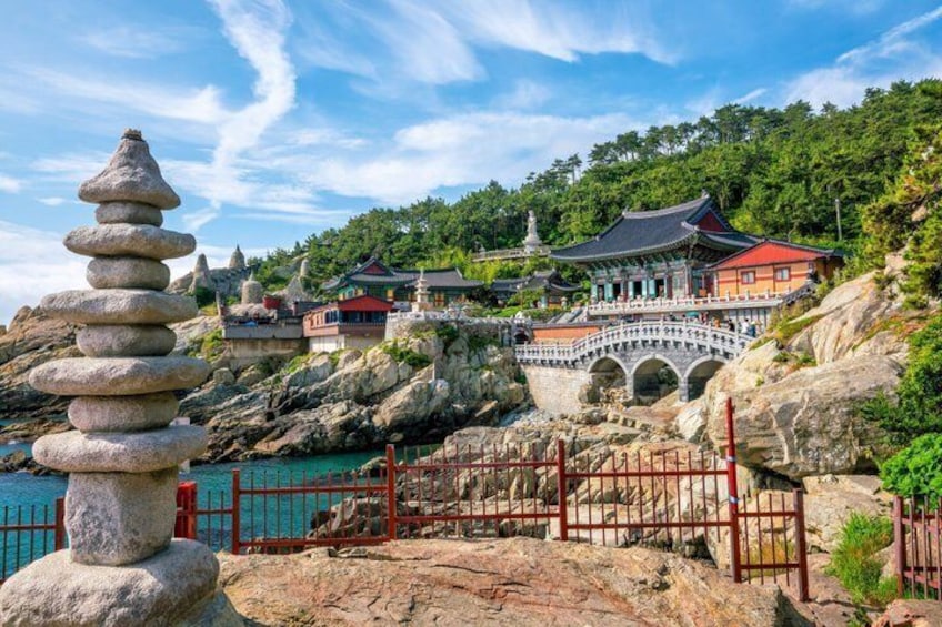 A traditional Korean temple with a stone stack, a bridge, and a red gate. 3