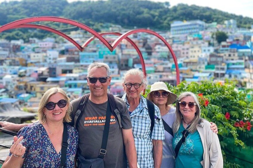 A group of people standing in front of a red arch structure with a cityscape in the background. 3