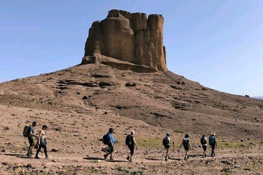 A group of hikers on a dirt trail with a large rock formation in the background. 1