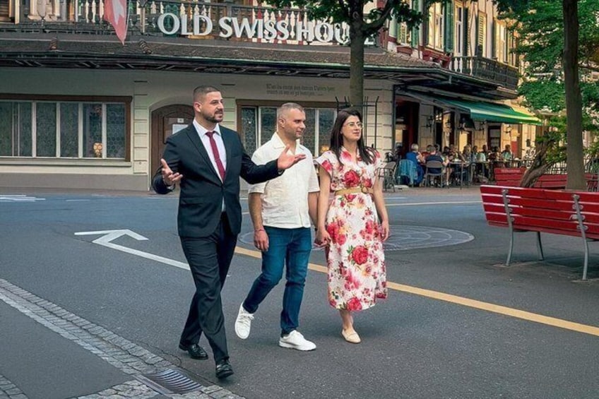 Three people walking on a street with a building labeled 'OLD SWISS HOUSE' in the background. 1