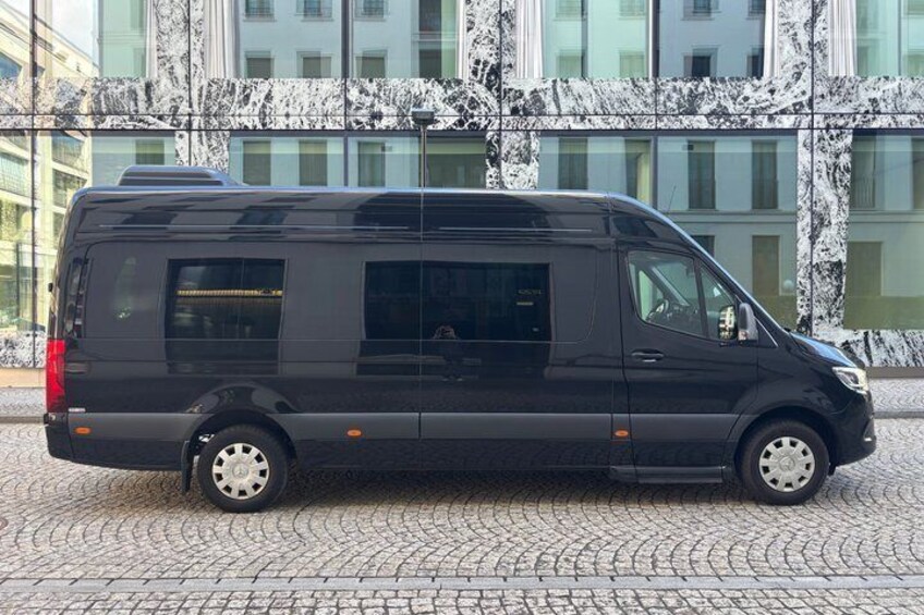 A black van parked on a cobblestone street in front of a building with a marble facade. 3