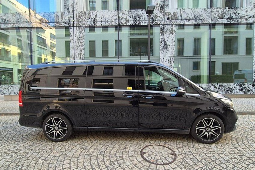 A black van parked on a cobblestone street in front of a building with a marble facade. 2