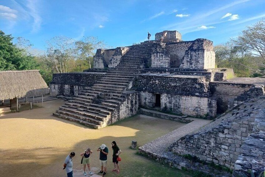 An ancient stone structure with steps leading up to a platform, surrounded by a grassy area and trees. 1