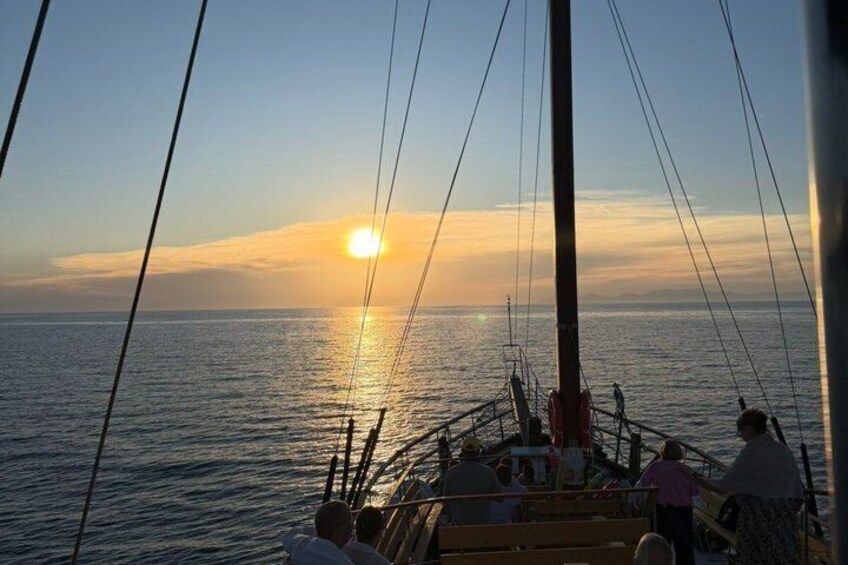 A sailboat with people on deck during sunset. 2