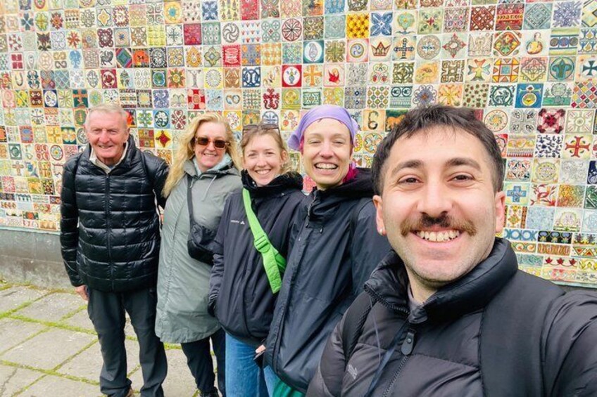 A group of people standing in front of a wall covered with colorful tiles. 3