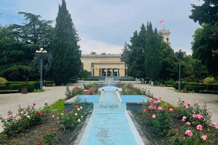 A formal garden with a central fountain, pathways, and a building with a flag. 3