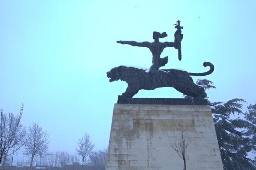 A statue of a figure on a horse, set on a pedestal, with trees and a clear sky in the background. 1