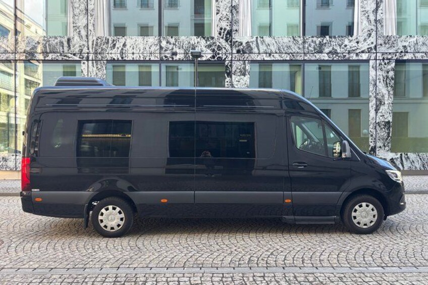 A black van parked on a cobblestone street in front of a building with a marble facade. 3